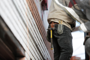 Construction worker installing metal roofing panels with tools on a residential structure
