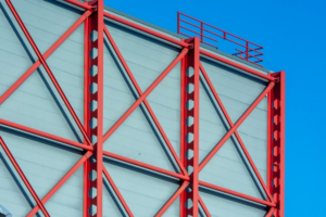 Red steel frame structure used in modern barndominium construction against blue sky