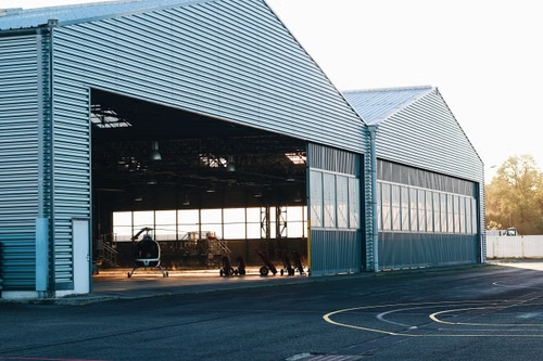 A modern industrial metal hangar exterior with a helicopter visible, offering spacious interior views