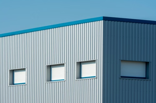 A sleek industrial building with a corrugated metal facade featuring roller blinds and sandwich panels