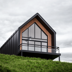 Sleek modern metal cabin design with glass facade and black metal frame on a lush green hillside.